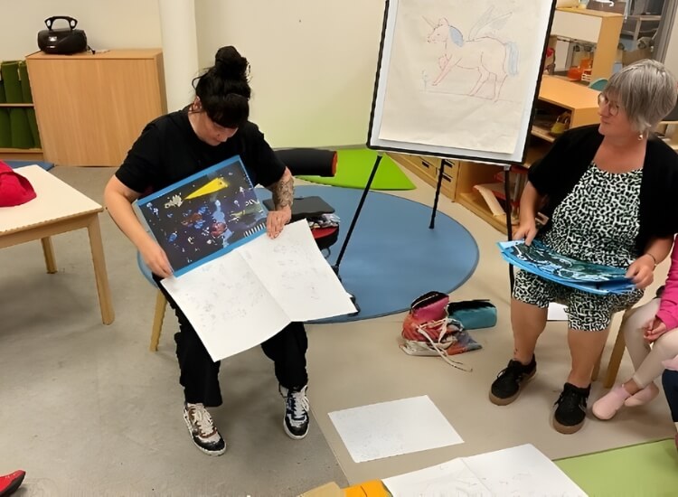 Kindergruppe sitzt um Illustratorin, die ihre Skizzen zeigt