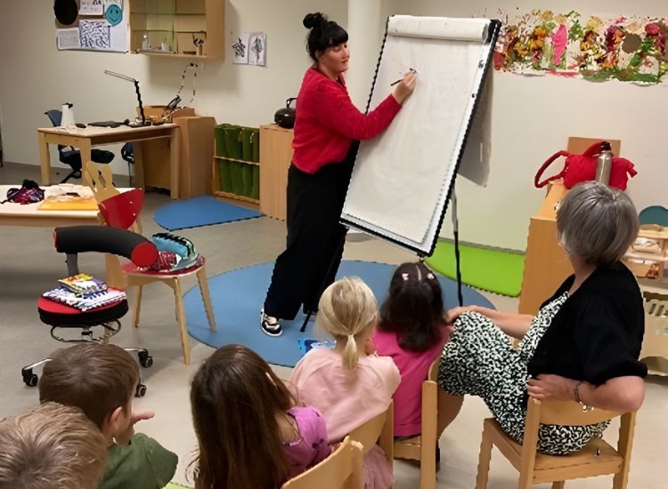 Kindergruppe sitzt um Illustratorin, die etwas malt