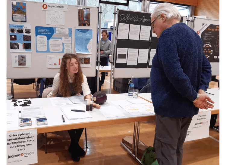 Mädchen an ihrem Infostand beim Wettbewerb Jugend forscht im Gespräch mit einem Besucher