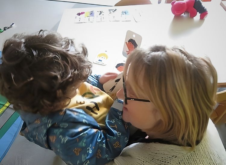 Deutsche Schule Toulouse: Erzieherin lächelt Kind an, das Karten in der Hand hat