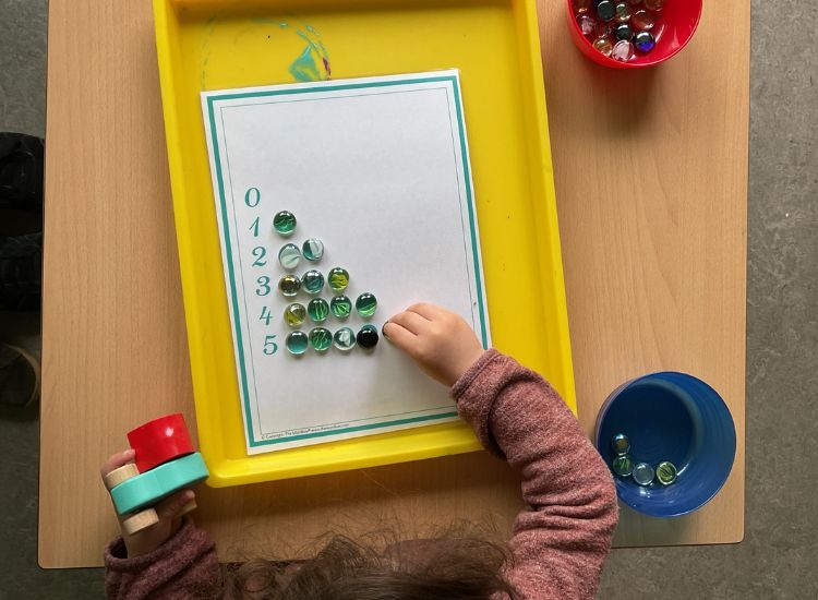 Kindergartenkind legt Zahlenmengen mit Glasperlen