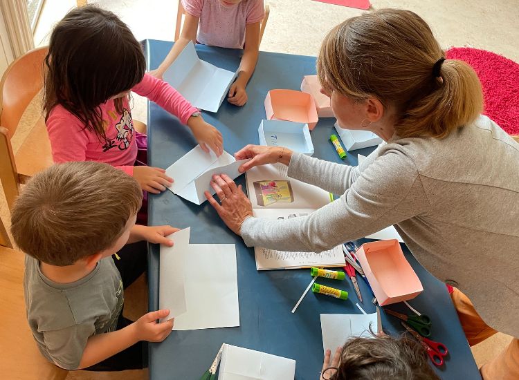 Erzieherin bastelt mit Kindern Papierboxen