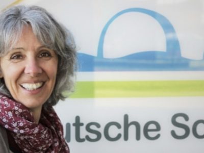 Portraitbild Dagmar Schröteler vor dem Logo der Deutschen Schule Toulouse